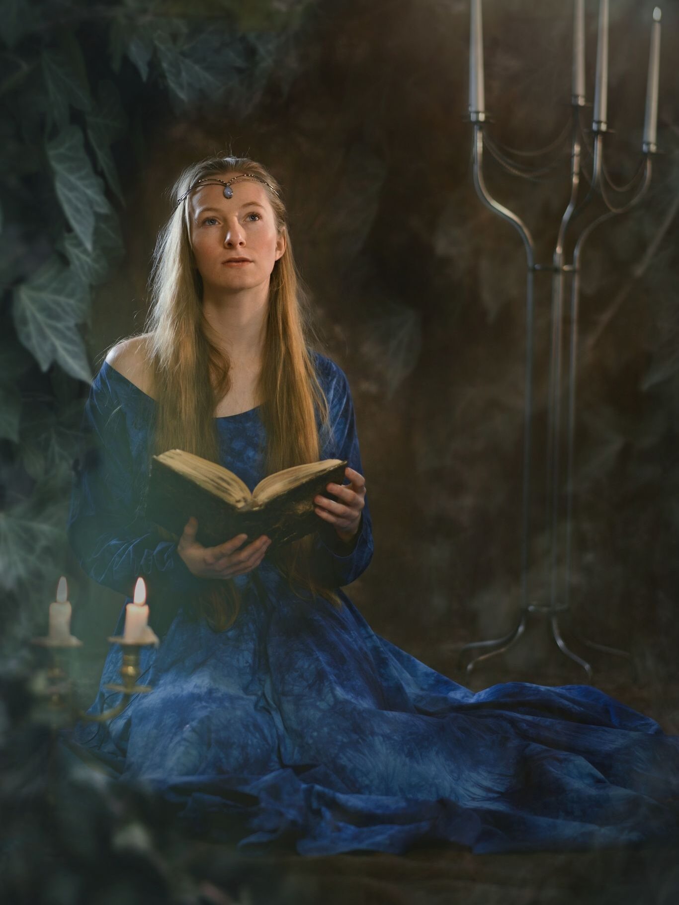 Žena v modrých fantasy šatech drží v ruce knihu.