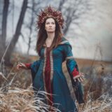 Žena ve středověkých šatech Femme petrolejové a vínové barvy se zlatým lemem.