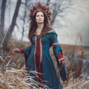 Žena ve středověkých šatech Femme petrolejové a vínové barvy se zlatým lemem.