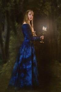Žena v modrých fantasy šatech drží v ruce svícen.