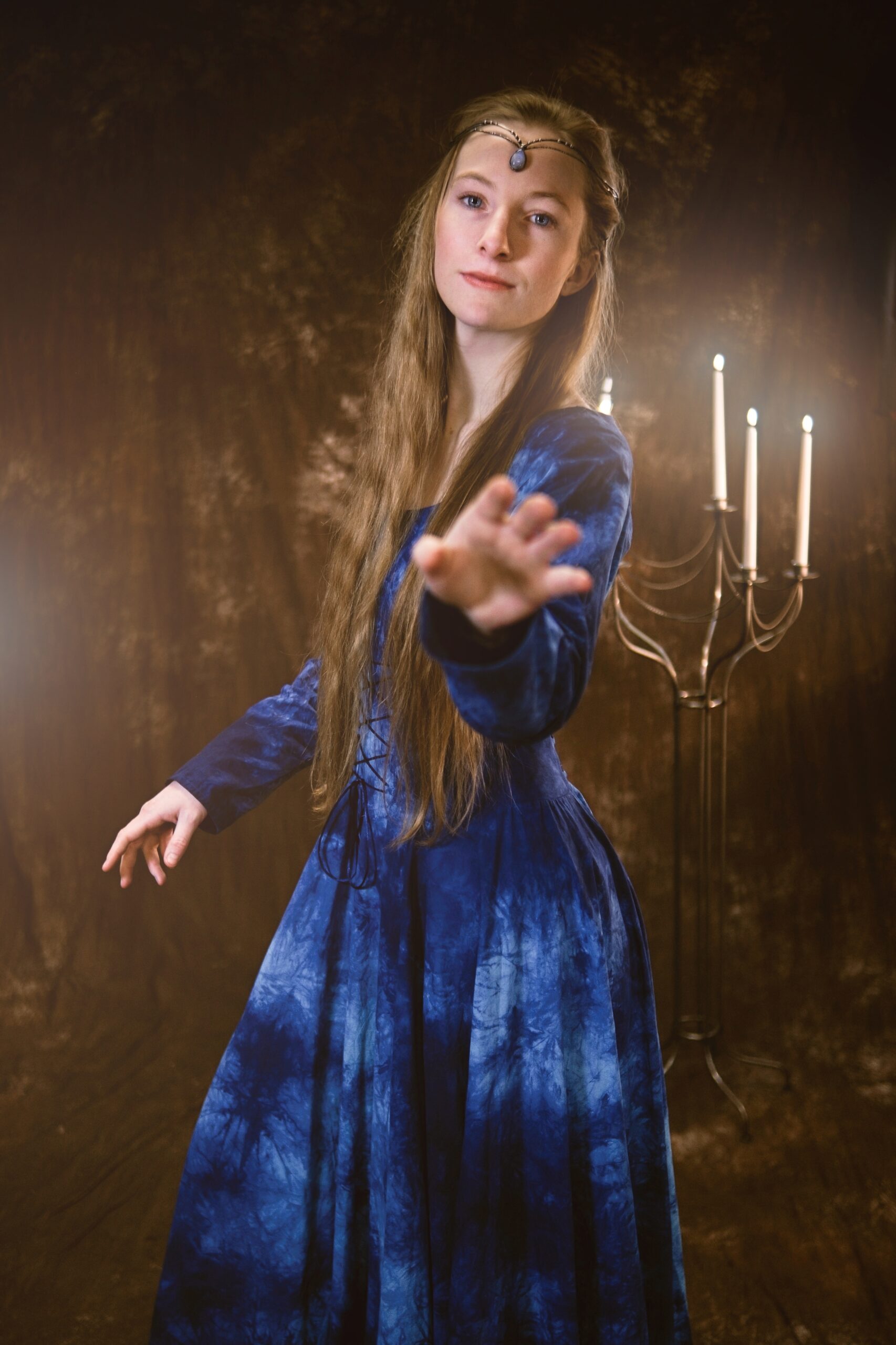 Žena v modrých fantasy šatech drží v ruce svícen.