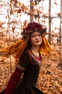 Krásná zrzavá žena ve fantasy šatech v podzimní krajině.