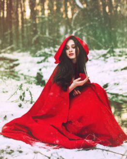 Žena v červeném vlněném plášti sedící v zimě u vody.