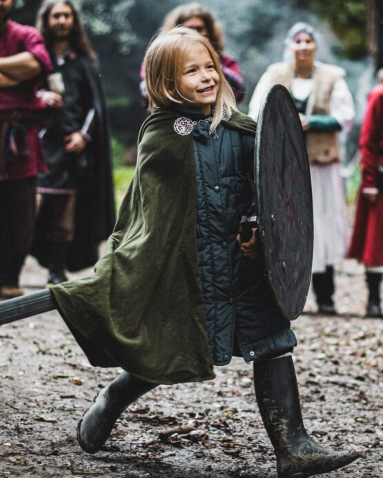 Malý kluk ve středověkém oděvu a vlněném plášti bojujíci se štítem a mečem.